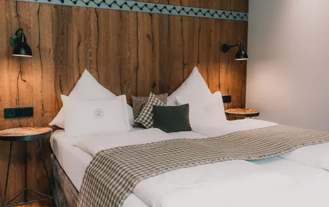 Die Pinzgauerin Gemütliches Hotelzimmer mit Doppelbett, Holzwand und moderner Beleuchtung